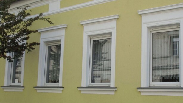 Ein Gebäude mit drei Fenstern, jeweils mit weißen Rahmen und einer Ziegelbasis.