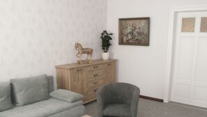 Ein Wohnzimmer mit grauem Sofa, einem grauen Sessel, einem Holztisch, einer Holzkommode, einer Topfpflanze und einem gerahmten Gemälde an der Wand.