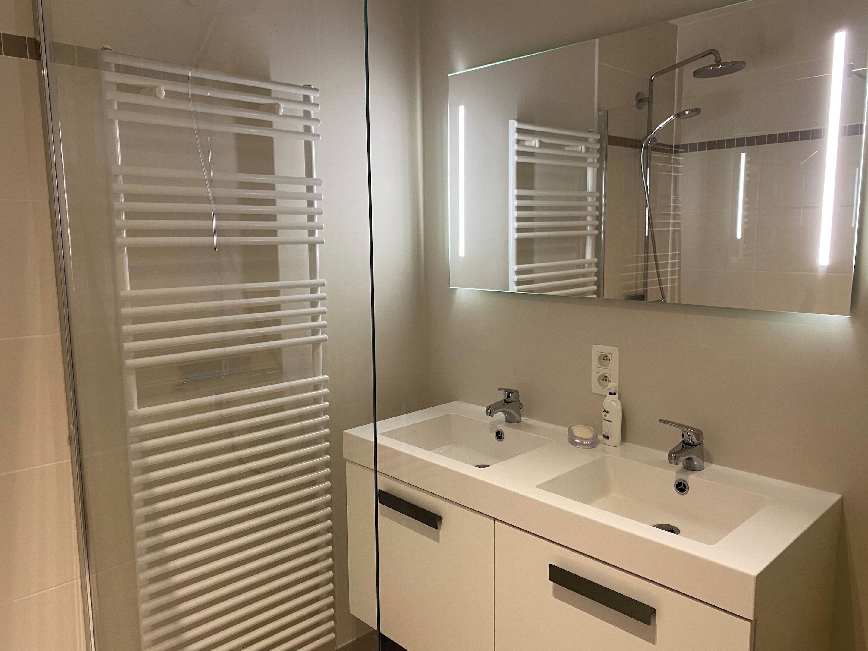 Ein modernes Badezimmer mit Glasdusche, doppelter Waschtisch und großem Spiegel.