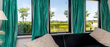 A room with a black sofa, green curtains, and a view of a garden.