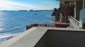 Ein Balkon mit Blick auf das Meer und eine entfernte Stadtlandschaft.