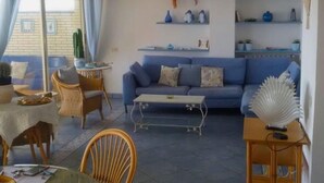 Ein Wohnzimmer mit einem blauen Sofa, einem Esstisch mit Stühlen und Regalen mit Dekoration.