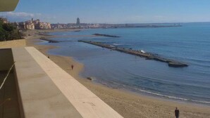 Eine Küstenansicht mit einer Uferpromenade, Strand und einer entfernten Stadtlandschaft.