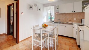 A kitchen with white cabinets, a sink, and a dining area with a table and chairs. - Apartment in Croatia Near the Coast (Marcana)