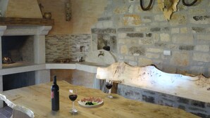 A rustic kitchen with a stone wall, a wooden table with a bottle of wine and a glass, and a hanging meat hook. - Apartment in Croatia Near the Coast (Marcana)