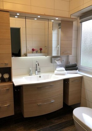 Un baño moderno con un lavamanos blanco, un espejo y armarios de madera.