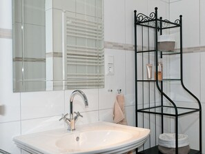 A bathroom with a sink, mirror, and a black metal shelf unit with toiletries. - Casa Schalkenmehren Grande (Schalkenmehren)
