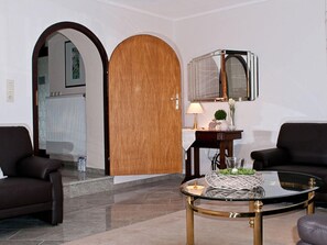 A modern living room with a glass coffee table, two dark sofas, a wooden door, and a small table with a lamp and decorative items. - Casa Schalkenmehren Grande (Schalkenmehren)