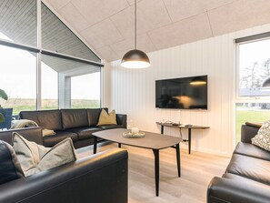 A modern living room with a large TV, leather sofas, a coffee table, and a view of the outdoors.