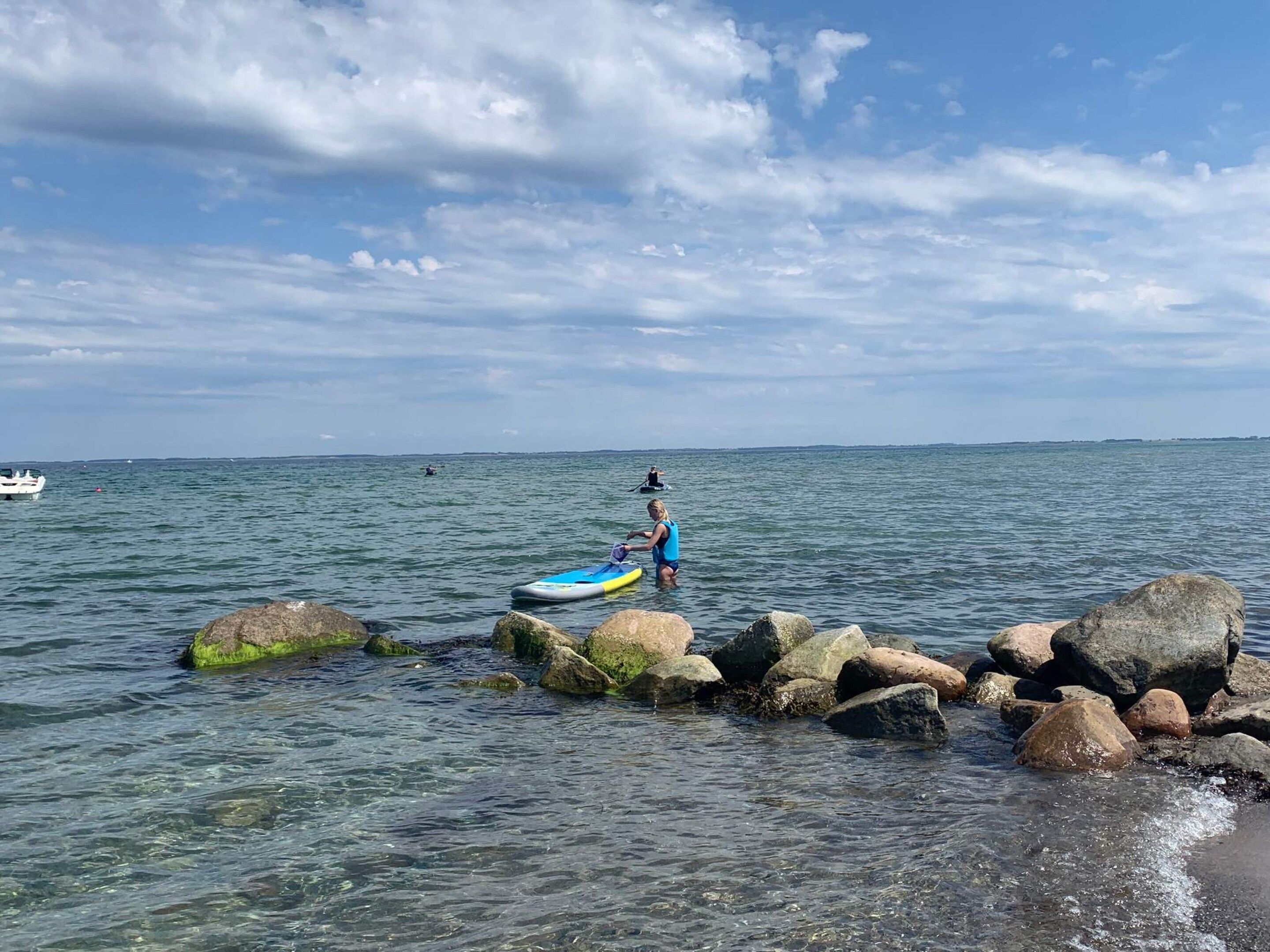 A calm sea with a kayak near rocks, a distant boat, and a clear sky.