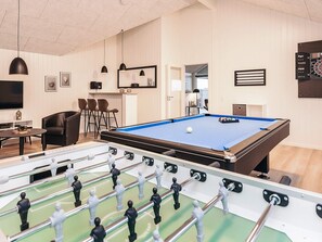 Une table de billard, avec une table de baby-foot devant, un téléviseur et des tableaux encadrés au mur.