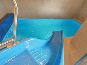 A blue slide in a pool area with a metal ladder and a tiled wall. - 5 Star Holiday Home in Otterup (Otterup)