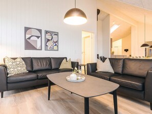 A modern living room with a dark leather sofa, a round coffee table, and abstract wall art. - 5 Star Holiday Home in Otterup (Otterup)