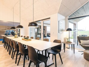 A modern dining area with a long table, black chairs, pendant lights, and a view of the outdoors.