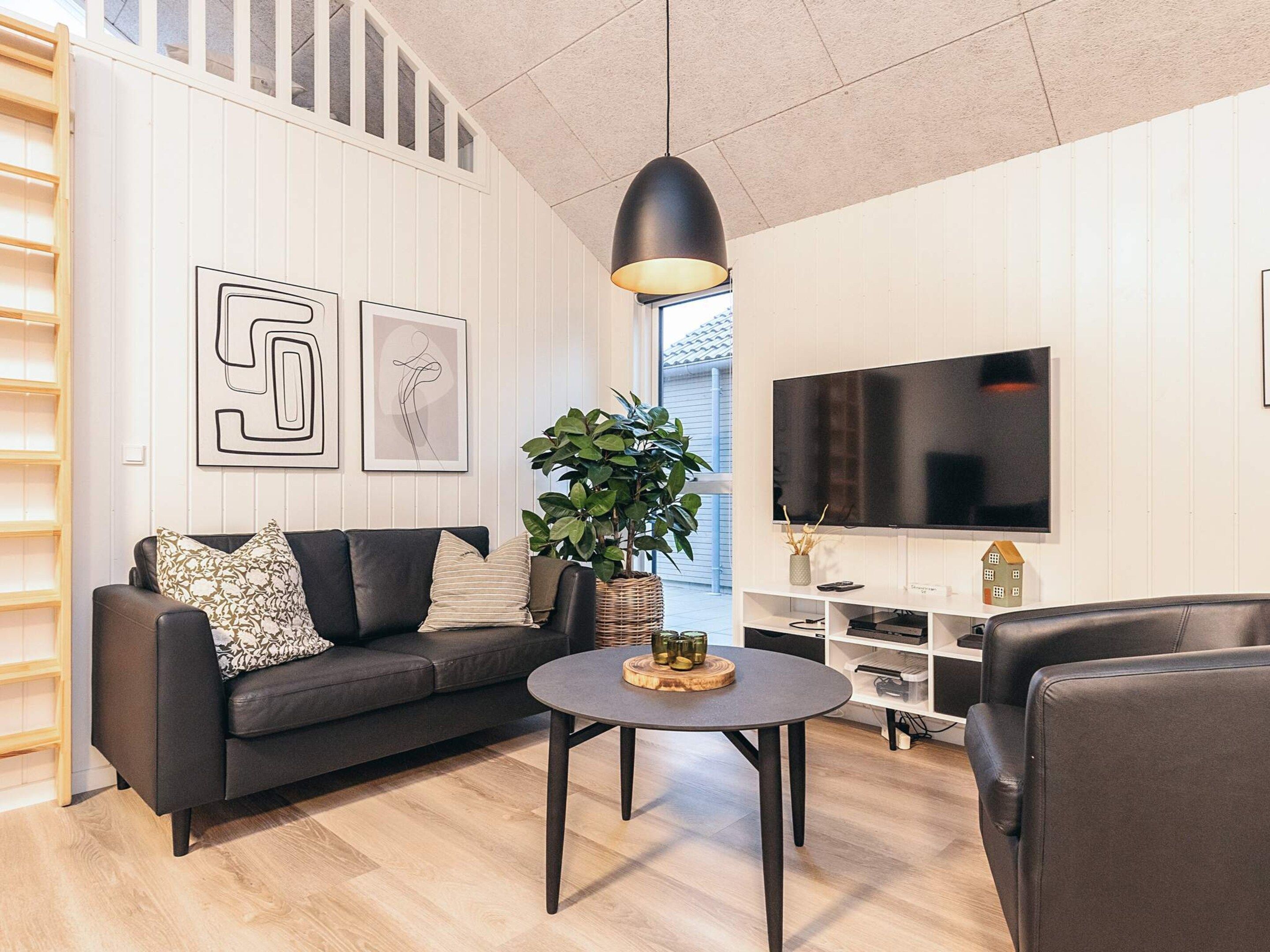 A modern living room with a black leather sofa, a round coffee table, and a large flat-screen TV.