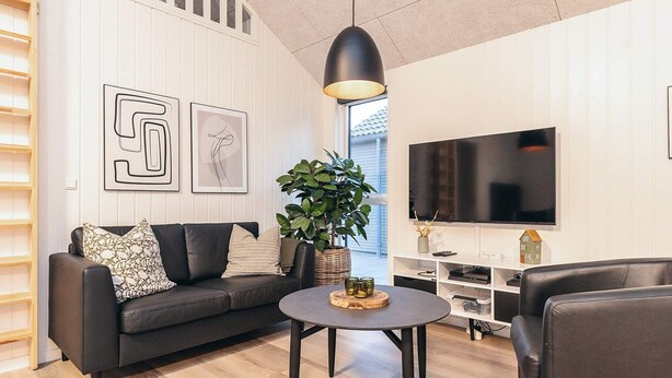 A modern living room with a black leather sofa, a round coffee table, and a large flat-screen TV. - 5 Star Holiday Home in Otterup (Otterup)