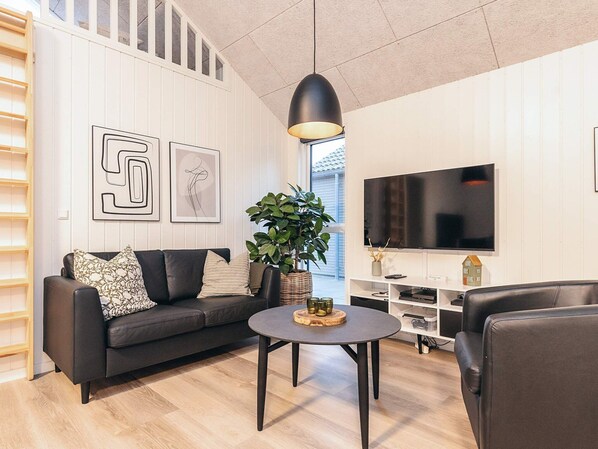 Un salon moderne avec un canapé en cuir noir, une table basse ronde et un grand téléviseur à écran plat.