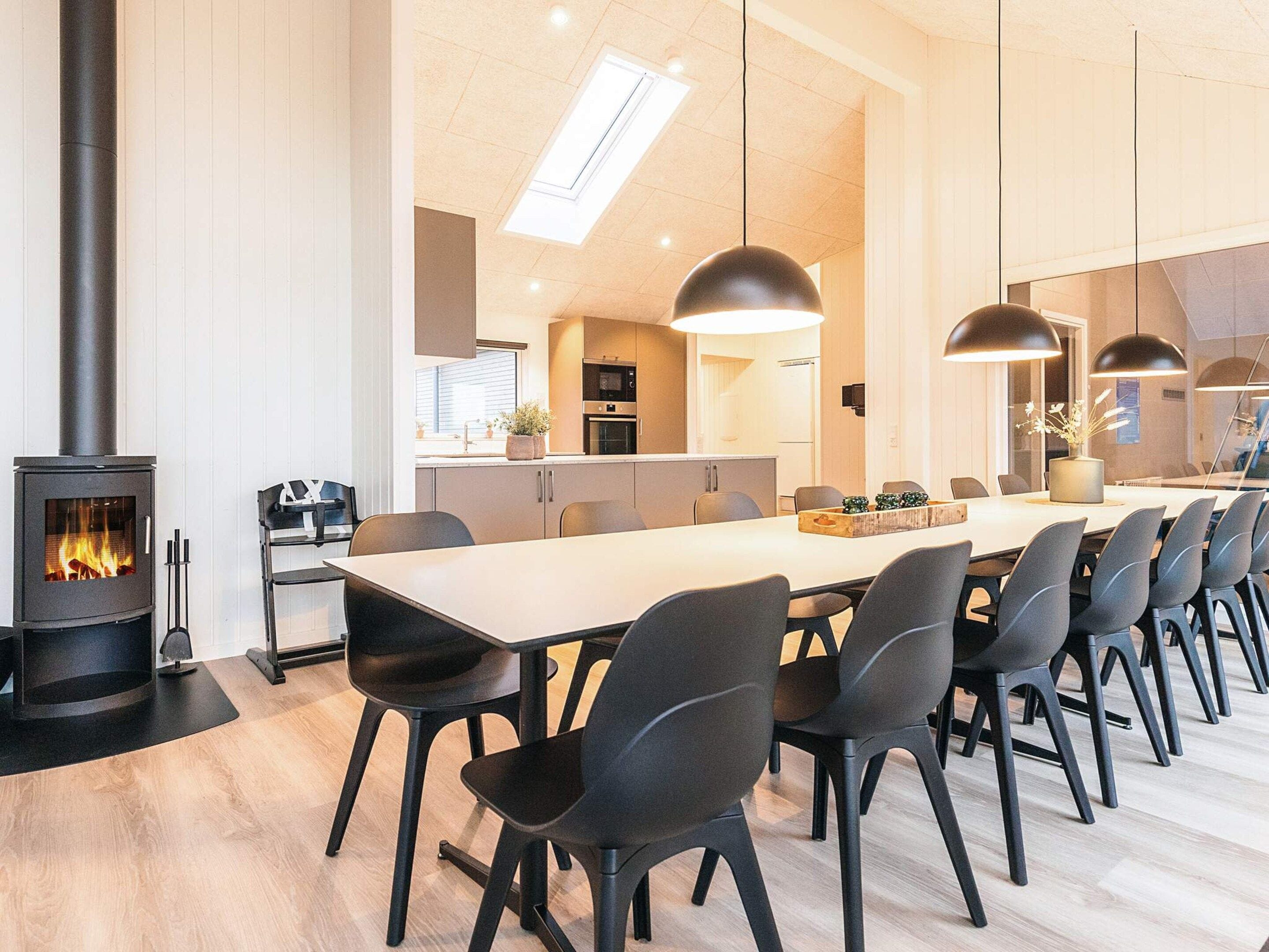 A modern kitchen with a central island, a dining area with a long table and chairs, and a wood-burning stove.