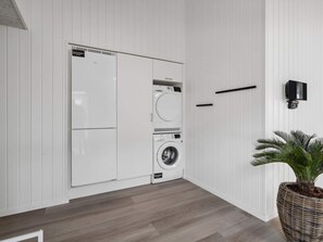 A laundry room with a white wall, a washing machine, a dryer, and a potted plant.