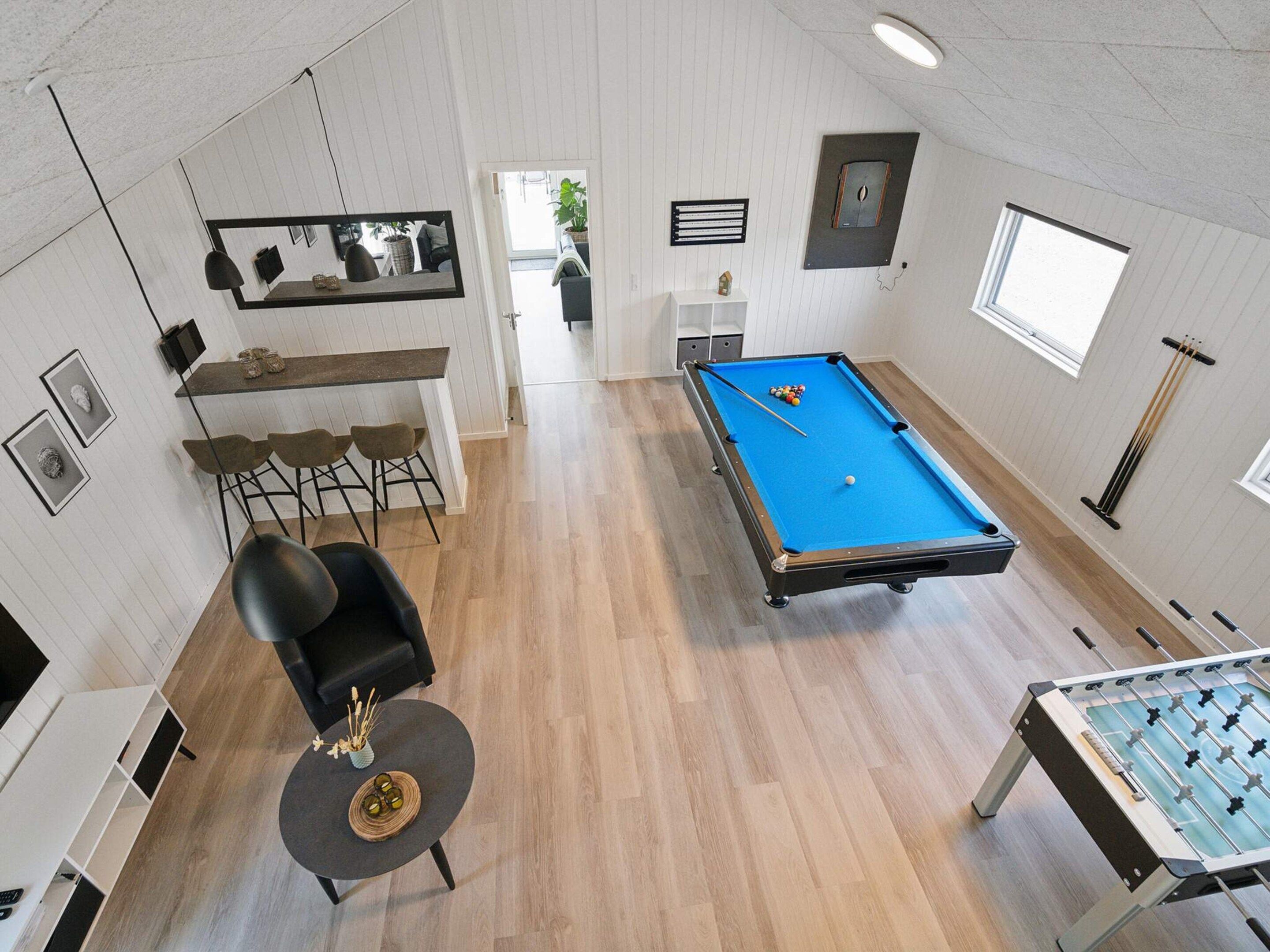 Une pièce équipée d’une table de billard, d’un baby-foot, d’un coin bar et d’un espace détente avec une chaise et une petite table.