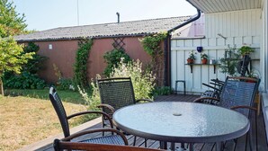 An outdoor patio with a round table and four chairs, surrounded by a wooden deck and a brick wall with climbing plants. - 4 Star Holiday Home in Visby (Visby)