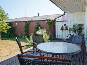 An outdoor patio with a round table and four chairs, surrounded by a wooden deck and a brick wall with climbing plants. - 4 Star Holiday Home in Visby (Visby)