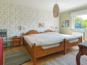 A bedroom with a wooden bed, floral wallpaper, a window with a view, and a hanging light fixture. - 4 Star Holiday Home in Visby (Visby)