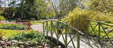 A wooden bridge over a garden with a variety of flowers and a stone wall in the background.