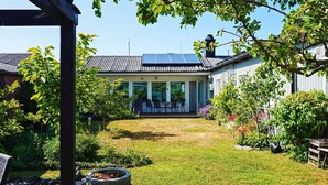 A covered patio area with a table and chairs, a stone fire pit, and a view of a house with a solar panel roof. - 4 Star Holiday Home in Visby (Visby)