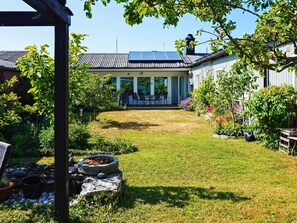 A covered patio area with a table and chairs, a stone fire pit, and a view of a house with a solar panel roof. - 4 Star Holiday Home in Visby (Visby)