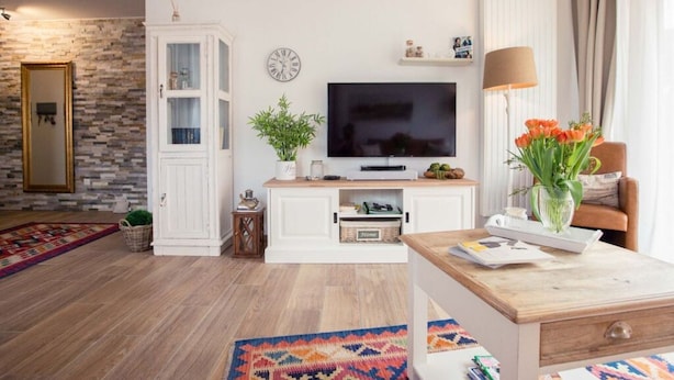 Un salon moderne avec un téléviseur à écran plat, un meuble blanc, une table basse en bois et un tapis coloré.