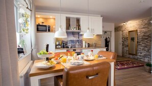 Une cuisine moderne avec des meubles blancs, un coin repas doté d’un fauteuil en cuir marron et un mur en pierre.