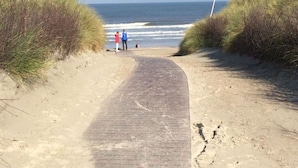Un sentier qui mène à la plage, avec du sable et de l’herbe de chaque côté.