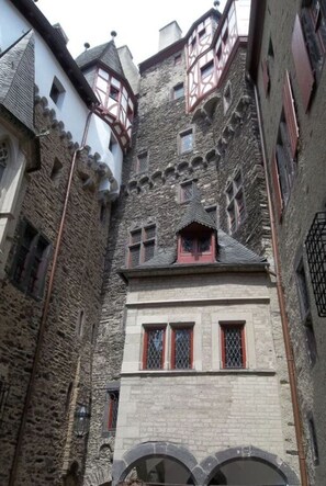 A narrow alleyway with stone buildings, one with a visible window and a small balcony.