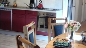 A kitchen with red cabinets, a stove, and a kettle. There is a dining table with chairs and a vase of flowers. - in Landhuisstijl met Uitzicht op de Moezel (Piesport)