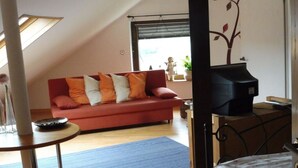 A cozy living room with a red sofa, a small table, a blue rug, a television, and a decorative plant. - in Landhuisstijl met Uitzicht op de Moezel (Piesport)