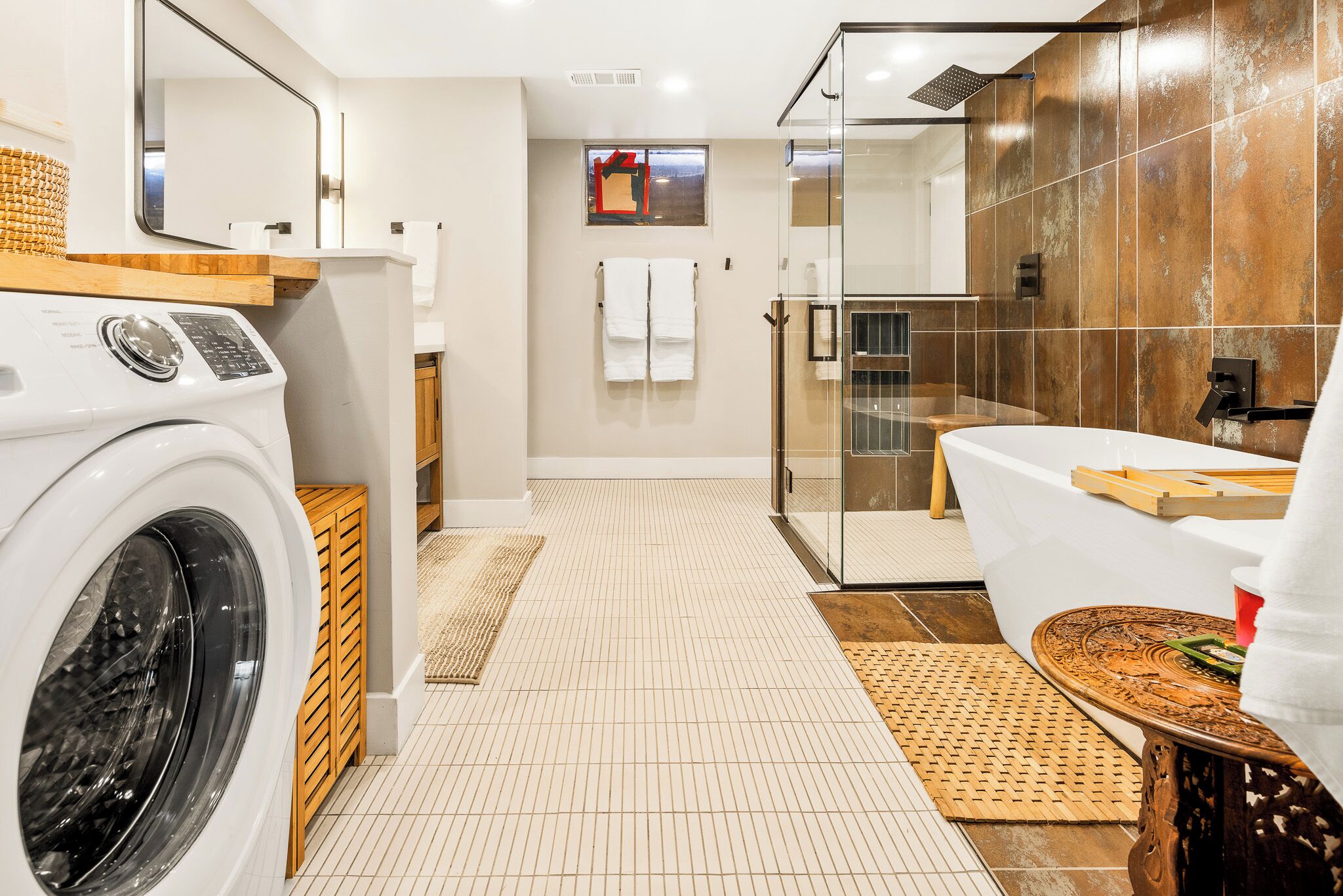 A modern bathroom with a washing machine, a glass shower enclosure, and a bathtub.