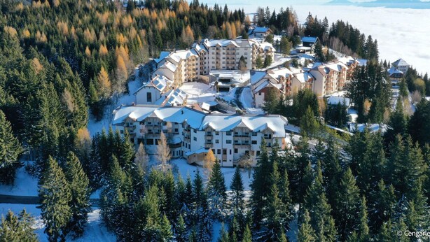 A snow-covered resort with multiple buildings, surrounded by dense forests and mountains in the background. - Holiday Apartment in Gerlitzen With Wellness Area (Treffen)