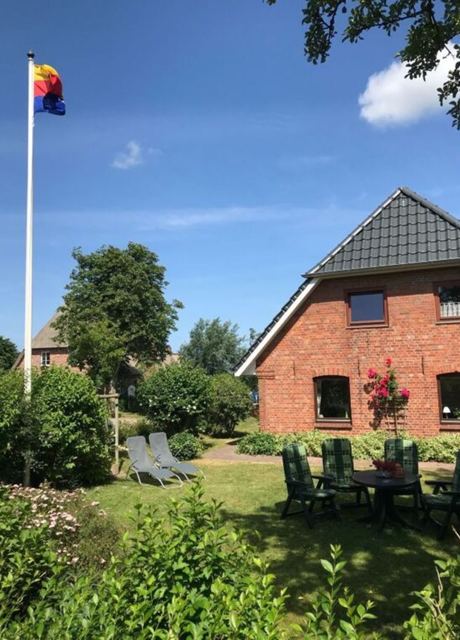 A brick building with a sloped roof, a flagpole with a flag, and a patio area with chairs and a table.