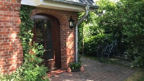 A brick house with a wooden door and window, a pathway leading to the entrance, and a bicycle parked outside. - Holiday Apartment Bruhn (Midlum)