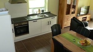 A compact kitchen with a sink, stove, and cabinets, a dining table with chairs, and a television in a wooden cabinet. - Holiday Home Manders (Wangerland)