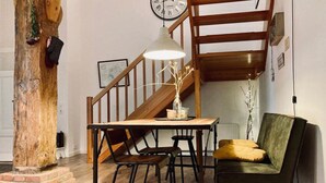 Un comedor con una mesa de madera, sillas y una lámpara colgante. Se ve una escalera al fondo.