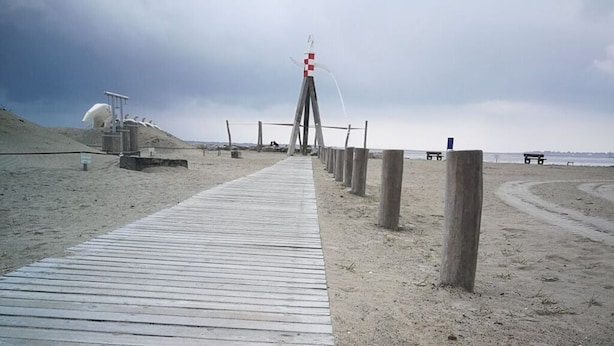 Una pasarela de madera que conduce a una torre de salvavidas en una playa arenosa.