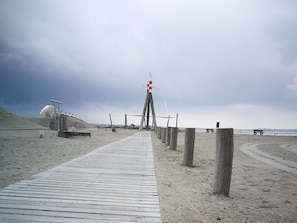 Une promenade en bois menant à un poste de surveillance des sauveteurs sur une plage de sable.