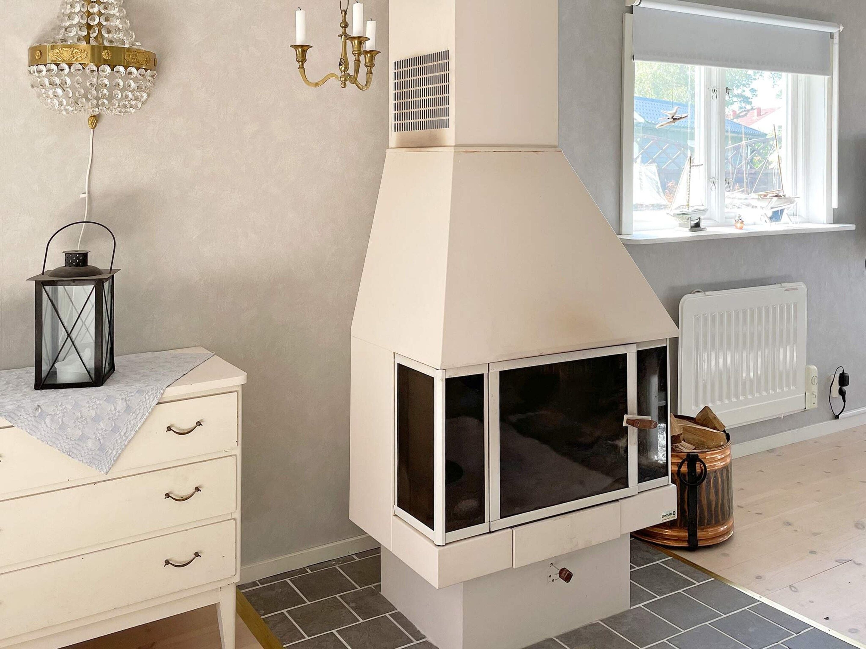 A room with a white fireplace, a window with a view of sailboats, a chandelier, and a lantern on a dresser.