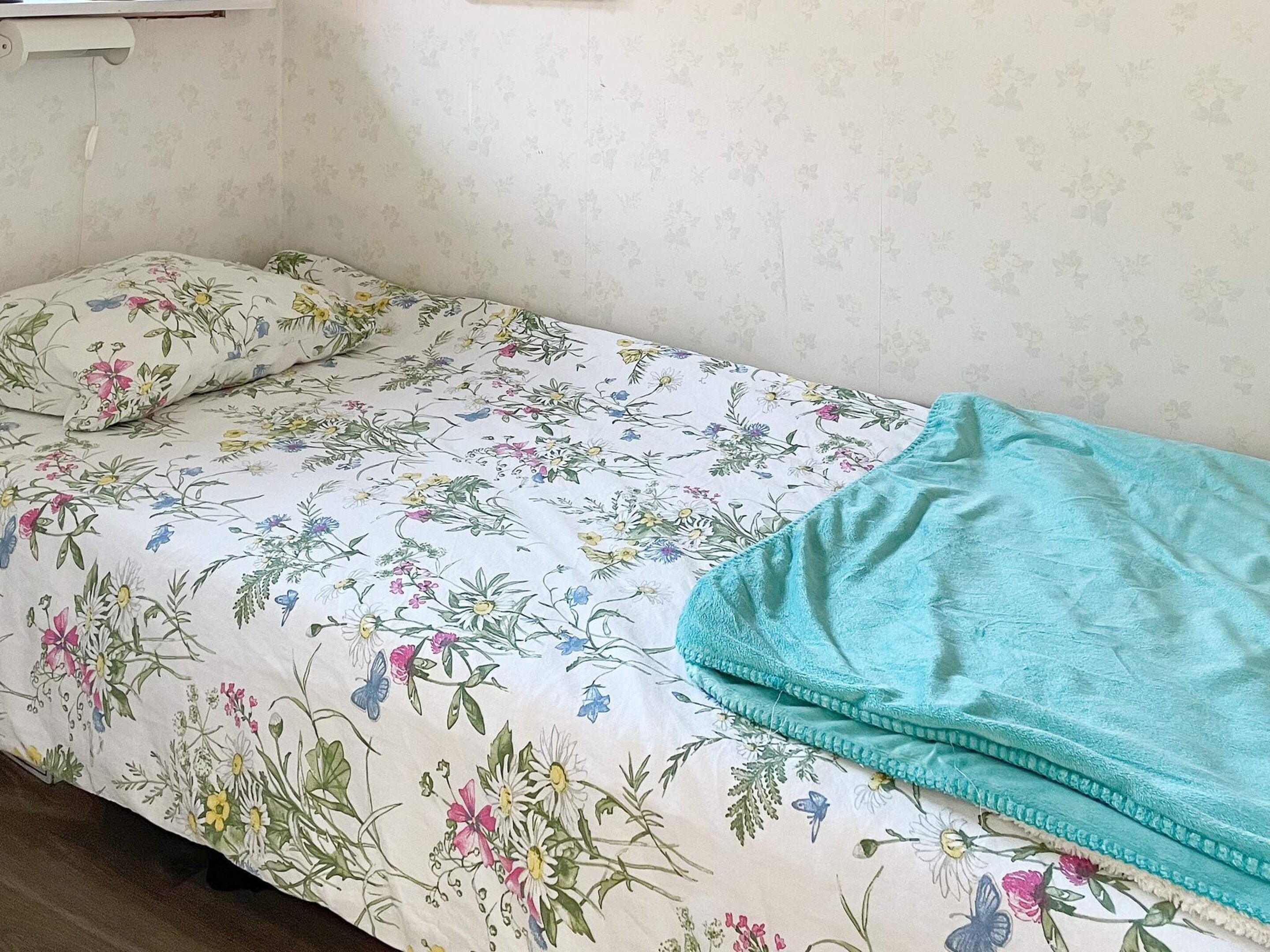 A single bed with a floral bedspread and a teal blanket.