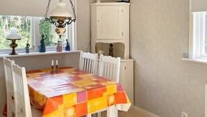 A dining area with a table covered in a colorful tablecloth, white chairs, a hanging lamp, and a white cabinet. - 4 Star Holiday Home in Solvesborg (Sölvesborg)
