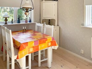 Ein Essbereich mit einem Tisch, der mit einer farbenfrohen Tischdecke bedeckt ist, weißen Stühlen, einer Pendelleuchte und einer weißen Kommode.