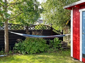 Eine Hängematte zwischen Bäumen, ein Holzzaun und ein rotes und blaues Gartenhaus.