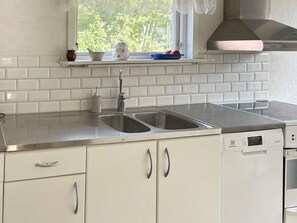 A kitchen with white cabinetry, a double sink, and a window with a view of trees.